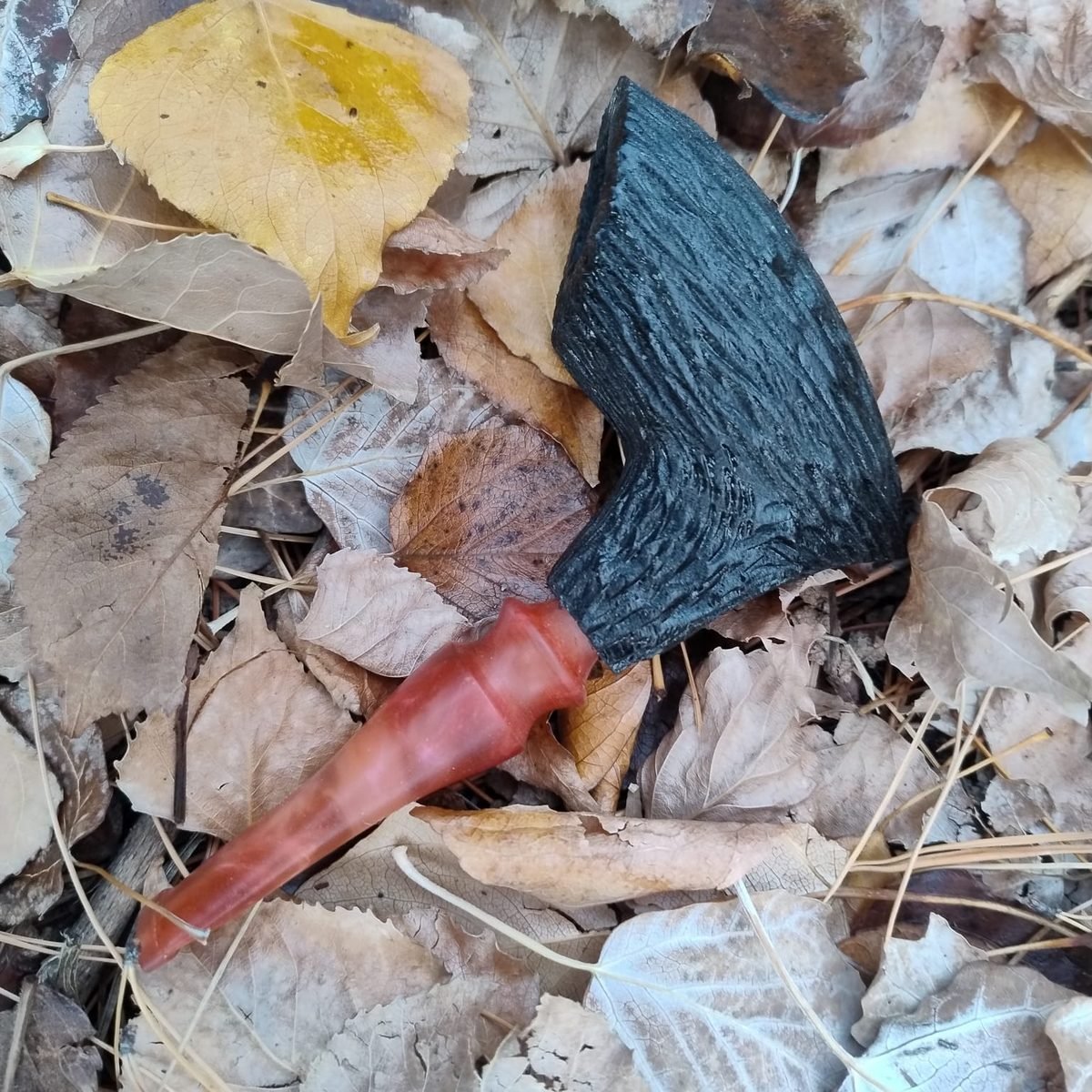 Pipa artesanal negra carbonizada entre hojas de otoño